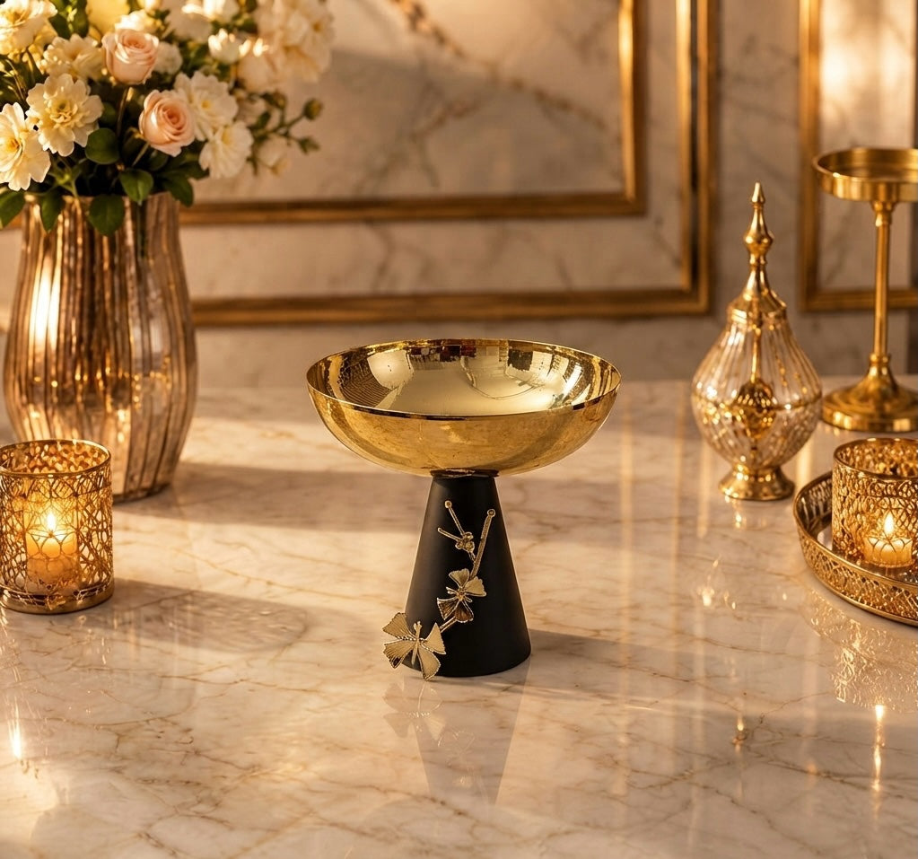 Home Sajawat decorative pedestal bowl with a hammered gold-tone finish and a matte black base featuring floral motifs.