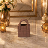 Home Sajawat handbag shaped ceramic tabletop vase in a soft mauve tone with a quilted texture on a marble surface.