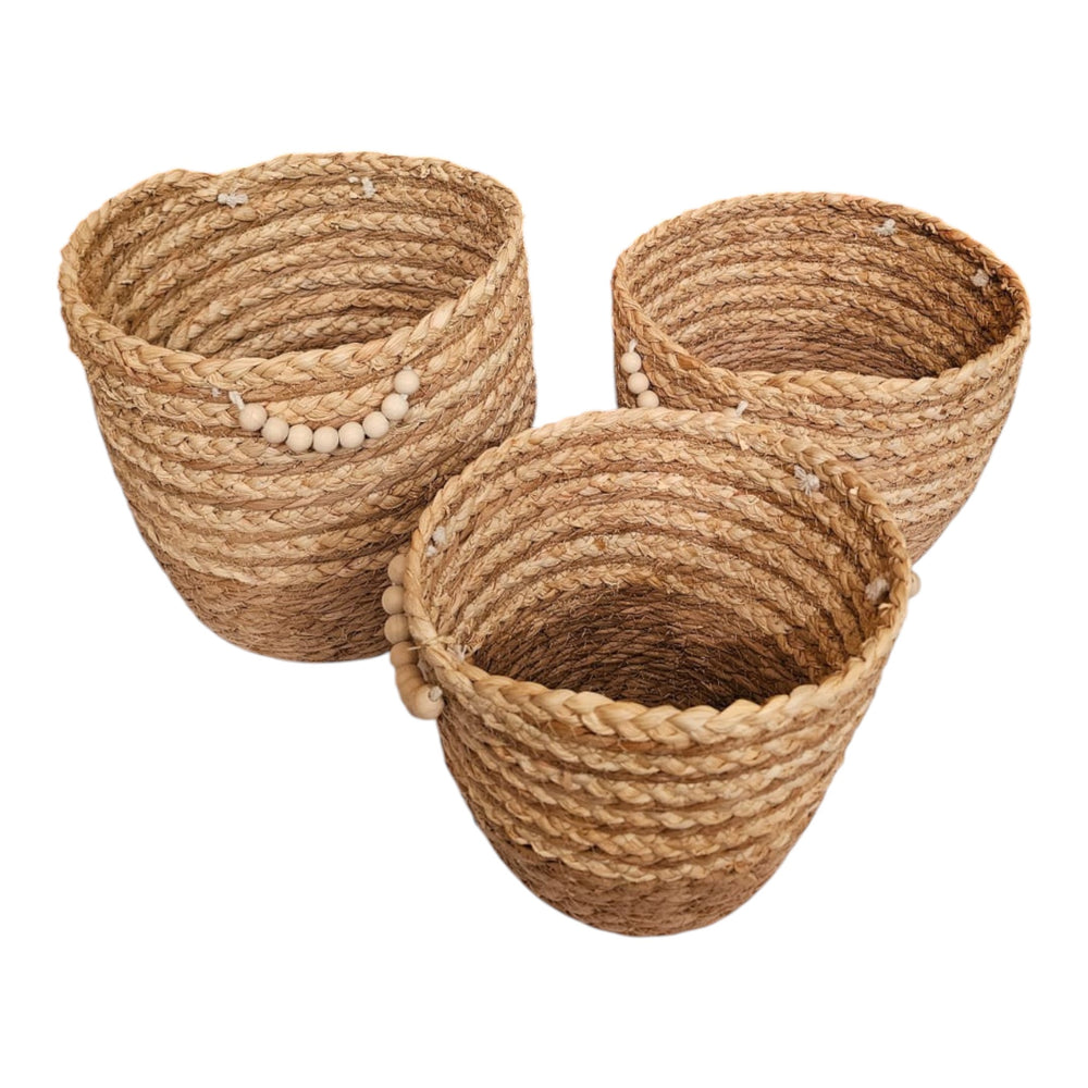 Home Sajawat set of three handwoven seagrass storage baskets with natural wooden bead accents on a white surface.