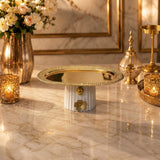 Home Sajawat pedestal serving tray with a polished gold-tone metal plate and a white fluted ceramic base with floral.