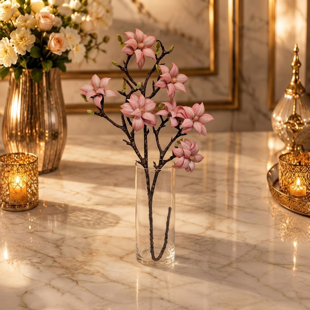 Home Sajawat artificial magnolia branch with soft pink flowers in a clear glass vase on a marble table.