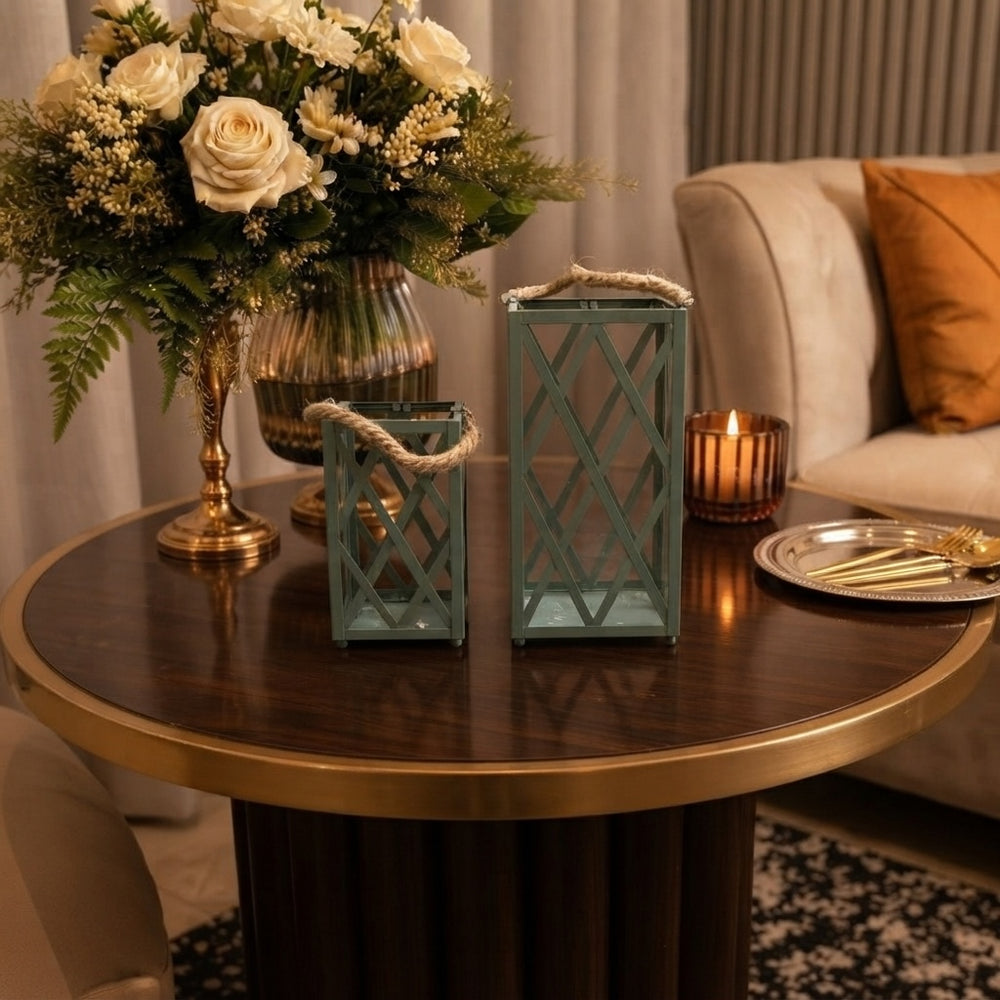 Home Sajawat set of two sage green metal lanterns with lattice patterns and rustic rope handles on a wooden table.