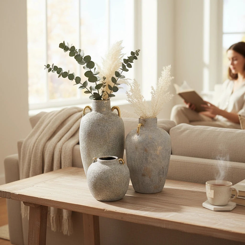 Home Sajawat set of three grey-blue textured ceramic amphora vases with gold handles and rims, holding dried pampas grass and eucalyptus.