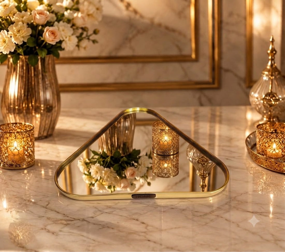 Home Sajawat triangular mirror serving tray with a polished gold metal frame on a marble table with candles.