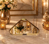 Home Sajawat triangular mirror serving tray with a polished gold metal frame on a marble table with candles.