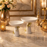 Home Sajawat white ceramic pedestal serving bowls with gold floral accents displayed on a marble table.